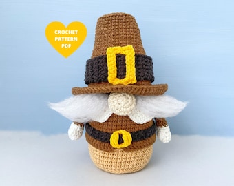 May include: Crocheted gnome wearing a brown hat with a yellow buckle and a brown and black belt with a yellow buckle. The gnome has a white beard and is standing on a light blue background.