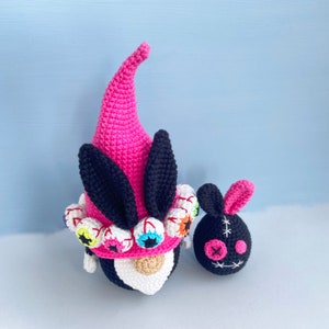 K&ouml;nnte beinhalten: Zwei geh&auml;kelte Gnome, einer rosa mit schwarzen Ohren und einem wei&szlig;en Gesicht mit bunten Augen, der andere schwarz mit einem gestickten Gesicht.