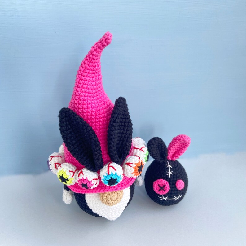 K&ouml;nnte beinhalten: Zwei geh&auml;kelte Gnome, einer rosa mit schwarzen Ohren und einem wei&szlig;en Gesicht mit bunten Augen, der andere schwarz mit einem gestickten Gesicht.