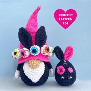 K&ouml;nnte beinhalten: Ein rosa und schwarzer geh&auml;kelter Zwerg mit einem Hut, der mit bunten Augen verziert ist. Neben dem Zwerg befindet sich ein kleinerer rosa und schwarzer geh&auml;kelter Hase mit einem gestickten Gesicht. Der Text "CROCHET PATTERN PDF" befindet sich in einem rosa Herz.