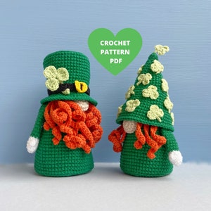 May include: Two crocheted gnomes wearing green hats with shamrock designs. One gnome has a red beard and the other has an orange beard. The gnomes are standing on a light blue background. CROCHET PATTERN PDF.