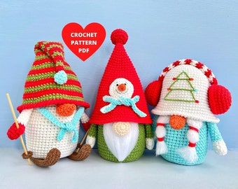 May include: Three crocheted gnomes with different hats and accessories. The gnome on the left has a red and green striped hat with a blue pom-pom, the middle gnome has a red hat with a white pom-pom and a blue bow, and the gnome on the right has a white hat with a green Christmas tree design and red earmuffs.