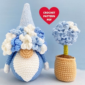 Puede incluir: Un gnomo de crochet con un gorro y una barba azul y blanca, sosteniendo una barba blanca en forma de corazón. El gnomo está de pie junto a un árbol de topiario de crochet azul y blanco en una maceta de color canela. El texto "CROCHET PATTERN PDF" está en un corazón rojo.