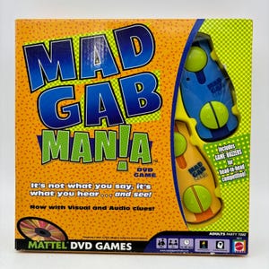 May include: A square board game box for Mad Gab Mania DVD game with an orange background featuring blue and green text. The box displays two plastic game buzzers in blue and yellow with green buttons, and includes the text It's not what you say, it's what you hear... and see!