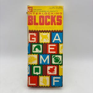 May include: A rectangular cardboard box for Halsam Hi-Lo American Safety Interlocking Blocks, set number 3221, containing 21 blocks. The yellow box features red and black text with a grid of colorful squares displaying letters and animal illustrations.