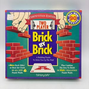 May include: A square board game box for Brick by Brick, a two-player competition edition building puzzle. The purple box features yellow text, red brick illustrations, and a yellow starburst graphic stating 90 all new puzzles included.