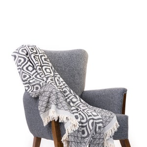 Puede incluir: Un sill&oacute;n gris con patas de madera y una manta de tiro con estampado en blanco y negro drapeada sobre el respaldo y el asiento.