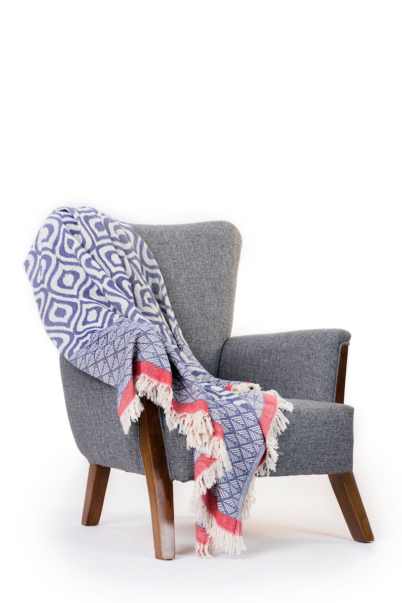 Puede incluir: Un sill&oacute;n gris con patas de madera y una manta de tiro azul y blanca con flecos rojos.