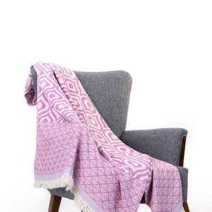 Puede incluir: Una manta de tiro de color rosa y blanco con estampado drapeada sobre un sill&oacute;n gris con patas de madera.
