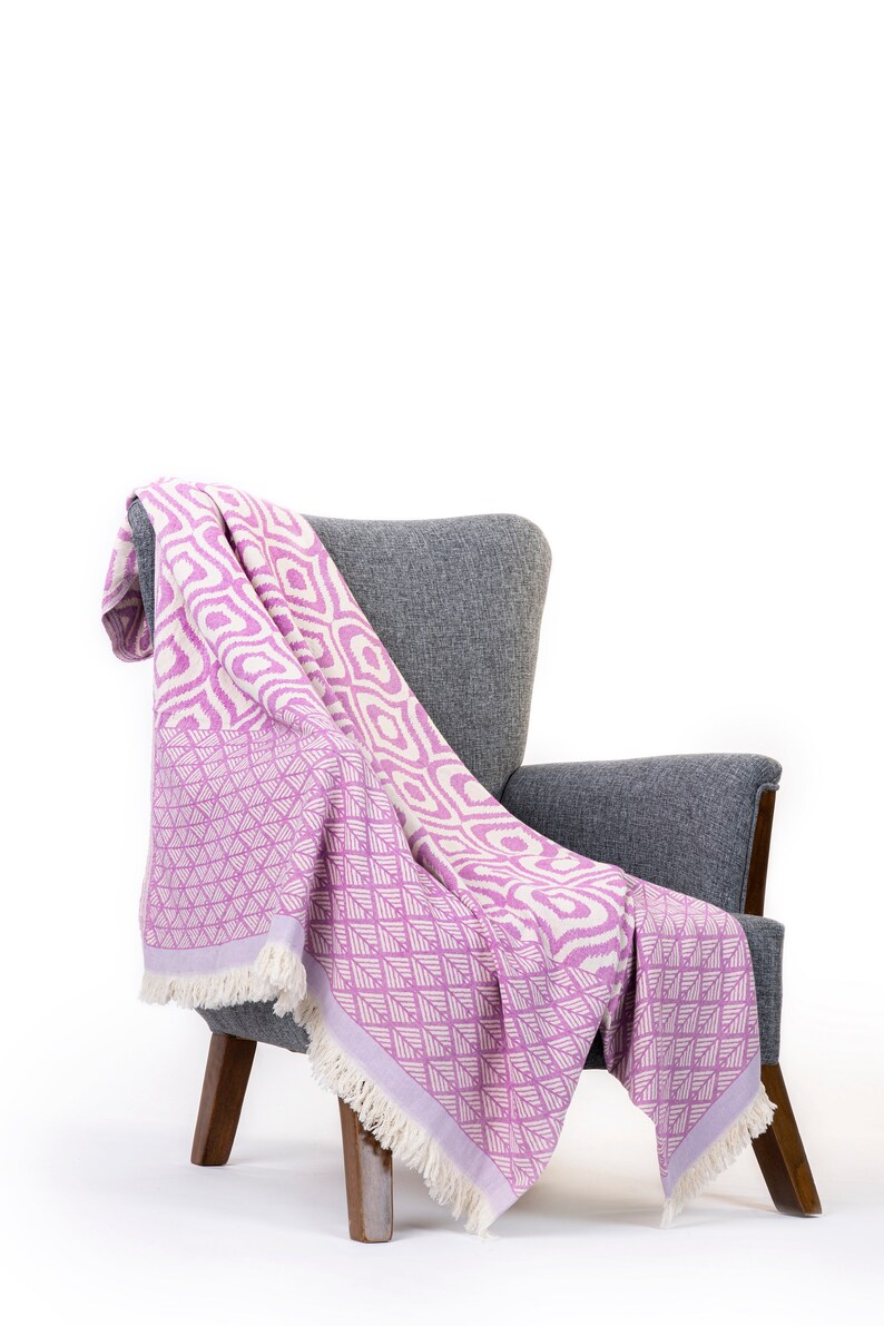 Puede incluir: Una manta de tiro de color rosa y blanco con estampado drapeada sobre un sill&oacute;n gris con patas de madera.