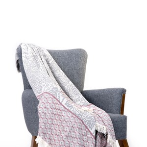 Puede incluir: Un sill&oacute;n gris con una manta de tiro blanca y gris drapeada sobre &eacute;l. La manta tiene un patr&oacute;n geom&eacute;trico rosa y blanco en la mitad inferior.