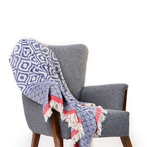Puede incluir: Un sill&oacute;n gris con patas de madera y una manta de tiro azul y blanca con ribetes rojos.