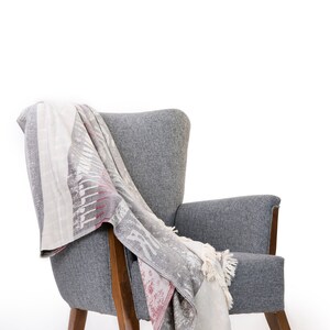 Puede incluir: Un sill&oacute;n gris con patas de madera y una manta de lana estampada sobre el respaldo y el asiento.