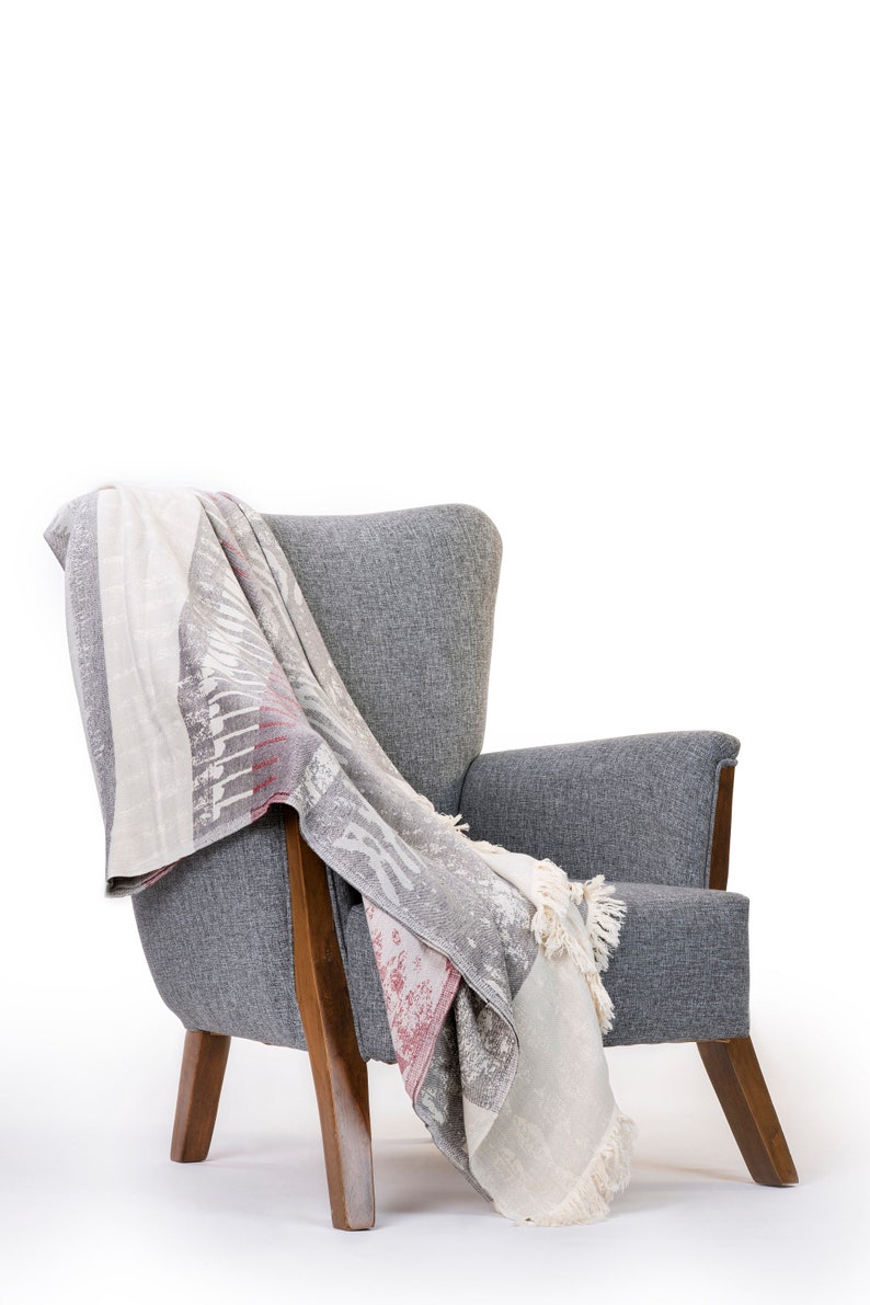 Puede incluir: Un sill&oacute;n gris con patas de madera y una manta de lana estampada sobre el respaldo y el asiento.