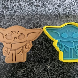 Può includere: Due stampini per biscotti a forma del personaggio Baby Yoda della serie Star Wars. Uno stampino è marrone e l'altro è blu con un contorno giallo.