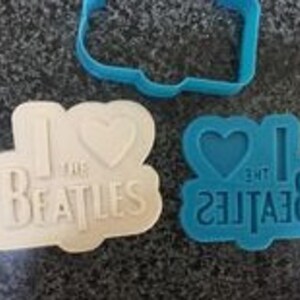 May include: Two cookie cutters, one blue and one white, shaped like the words "I love the Beatles" with a heart in place of the word "love".