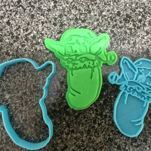 Può includere: Tre stampini per biscotti a forma di un personaggio che indossa un cappello da Babbo Natale. Gli stampini sono verdi, blu e blu chiaro.