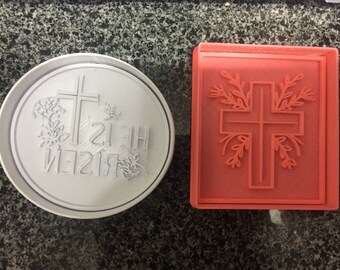 May include: Two white and red plastic cookie cutters, one with a cross and the words "He is Risen" and the other with a cross and floral designs.