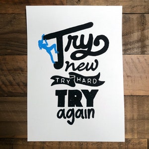 May include: A white poster with black text that reads "Try new try hard try again". A blue silhouette of a person climbing is in the upper left corner.