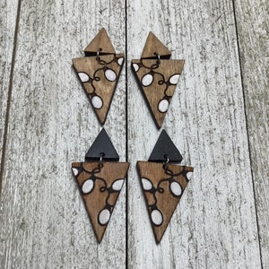 May include: A pair of wooden triangle earrings with a black triangle accent. The earrings are decorated with a white string of lights design.