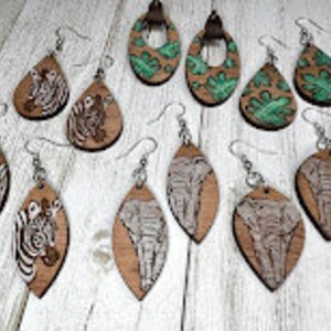 May include: Assortment of eight wooden dangle earrings with various animal and leaf designs. The earrings are in the shapes of teardrops and ovals. The designs include zebra, elephant, and green leaves.