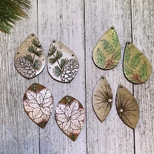 May include: Eight wooden earrings with various designs.  The designs include pine cones, holly leaves, poinsettias, and a geometric pattern.  The earrings are all in shades of green, brown, and white.