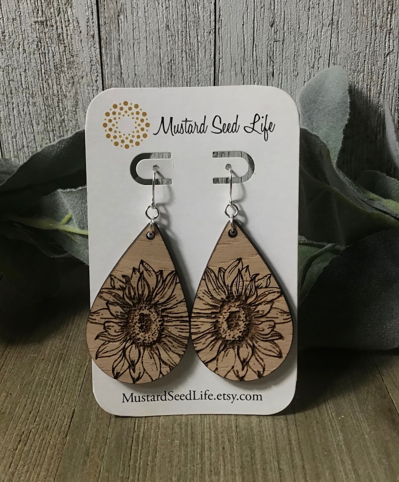 Peut inclure: Une paire de boucles d'oreilles en bois en forme de goutte d'eau avec un motif de tournesol grav&eacute; au laser. Les boucles d'oreilles sont sur une carte blanche avec le texte "Mustard Seed Life" et "MustardSeedLife.etsy.com".