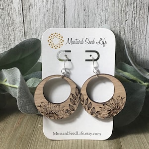 Peut inclure: Une paire de boucles d'oreilles en bois avec un motif de tournesol et de feuilles. Les boucles d'oreilles sont sur une carte blanche avec le texte "Mustard Seed Life" et "MustardSeedLife.etsy.com".