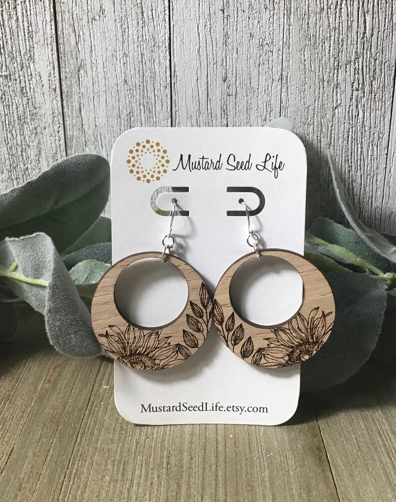 Peut inclure: Une paire de boucles d'oreilles en bois avec un motif de tournesol et de feuilles. Les boucles d'oreilles sont sur une carte blanche avec le texte "Mustard Seed Life" et "MustardSeedLife.etsy.com".