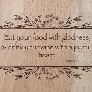 May include: A wooden chopping board with a laser-engraved quote: "Eat your food with gladness, & drink your wine with a joyful heart" and the reference "Ecclesiastes 9:7".