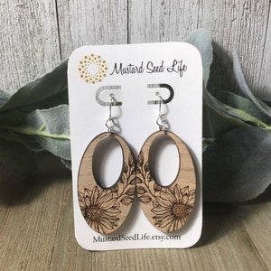 Peut inclure: Une paire de boucles d'oreilles en bois avec un motif de tournesol. Les boucles d'oreilles sont de forme ovale et ont une d&eacute;coupe au centre. Les boucles d'oreilles sont sur une carte blanche avec le texte "Mustard Seed Life" et "MustardSeedLife.etsy.com".
