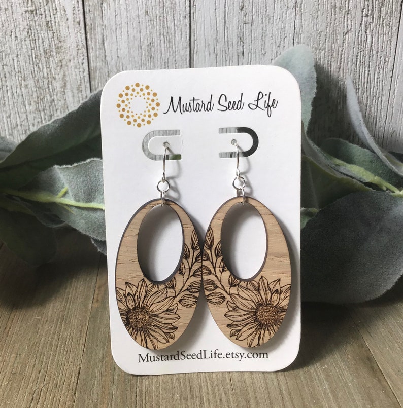 Peut inclure: Une paire de boucles d'oreilles en bois avec un motif de tournesol. Les boucles d'oreilles sont de forme ovale et ont une d&eacute;coupe au centre. Les boucles d'oreilles sont sur une carte blanche avec le texte "Mustard Seed Life" et "MustardSeedLife.etsy.com".