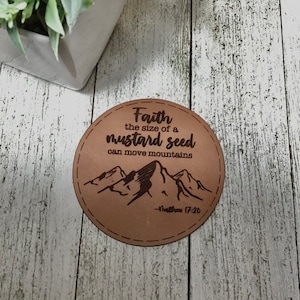 May include: A brown leather coaster with the text "Faith the size of a mustard seed can move mountains - Matthew 17:20" and a silhouette of mountains.