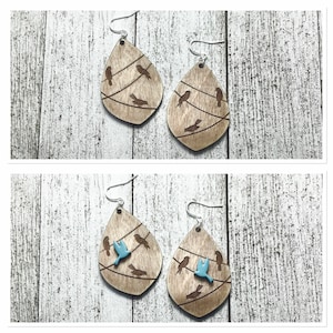 Op de afbeelding: Houten druppelvormige oorbellen met een vogel-op-draad-ontwerp. De oorbellen hebben een natuurlijke houtnerf afwerking met geëtste lijnen en vogel silhouetten. Eén paar heeft twee blauwe vogelaccenten.