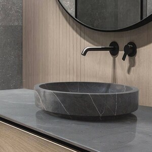 May include: A round, gray stone sink with a white marble pattern sits on a gray countertop. The sink is in a modern bathroom with a black faucet and a round mirror.