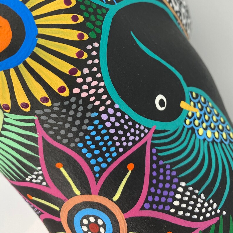 May include: A black ceramic vase with a colorful hand-painted design. The design features a bird with a blue body and yellow accents, surrounded by flowers and geometric patterns in shades of pink, blue, green, yellow, and white.