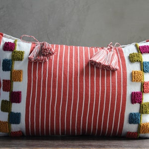 May include: Red and white striped lumbar pillow with colorful embroidered squares and tassels on each end.