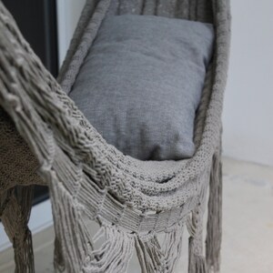 Puede incluir: Una hamaca gris con detalles de flecos. La hamaca est&aacute; hecha de un material tejido y tiene una almohada gris en su interior.