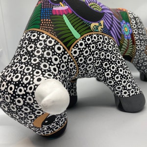 May include: Black and white ceramic bull figurine with a white nose and a colorful floral design on the back. The bull is painted with a black and white polka dot pattern.
