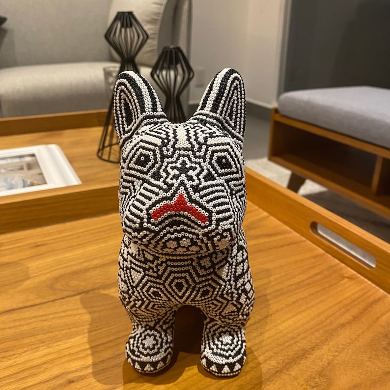 May include: A black and white beaded dog figurine with red detailing on the nose. The figurine is sitting on a wooden surface.