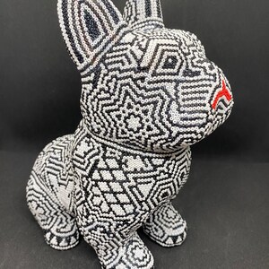 May include: A black and white beaded sculpture of a dog. The dog is sitting with its head turned to the side. The beads are arranged in a geometric pattern.