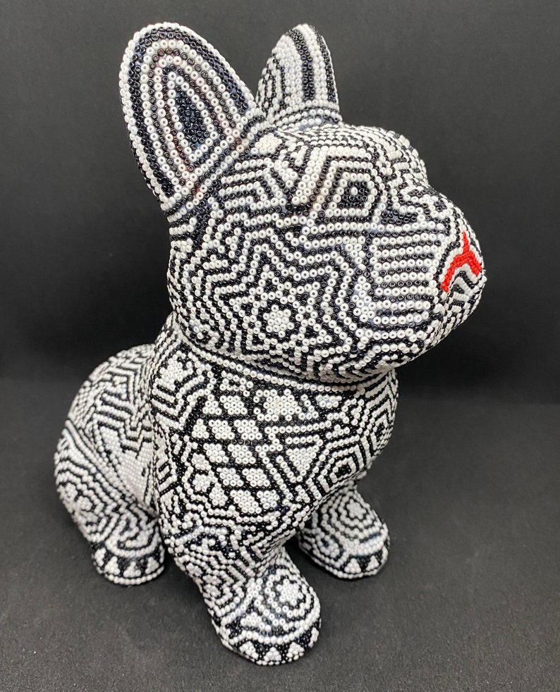 May include: A black and white beaded sculpture of a dog. The dog is sitting with its head turned to the side. The beads are arranged in a geometric pattern.