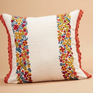 May include: White pillow with a red crocheted border and embroidered floral designs in shades of yellow, orange, red, pink, and blue.