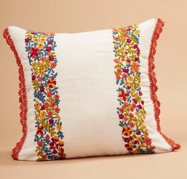 May include: White pillow with a red crocheted border and embroidered floral designs in shades of yellow, orange, red, pink, and blue.