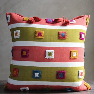 May include: A square throw pillow with a red, white, and green striped pattern. The pillow has colorful embroidered squares in a geometric design.