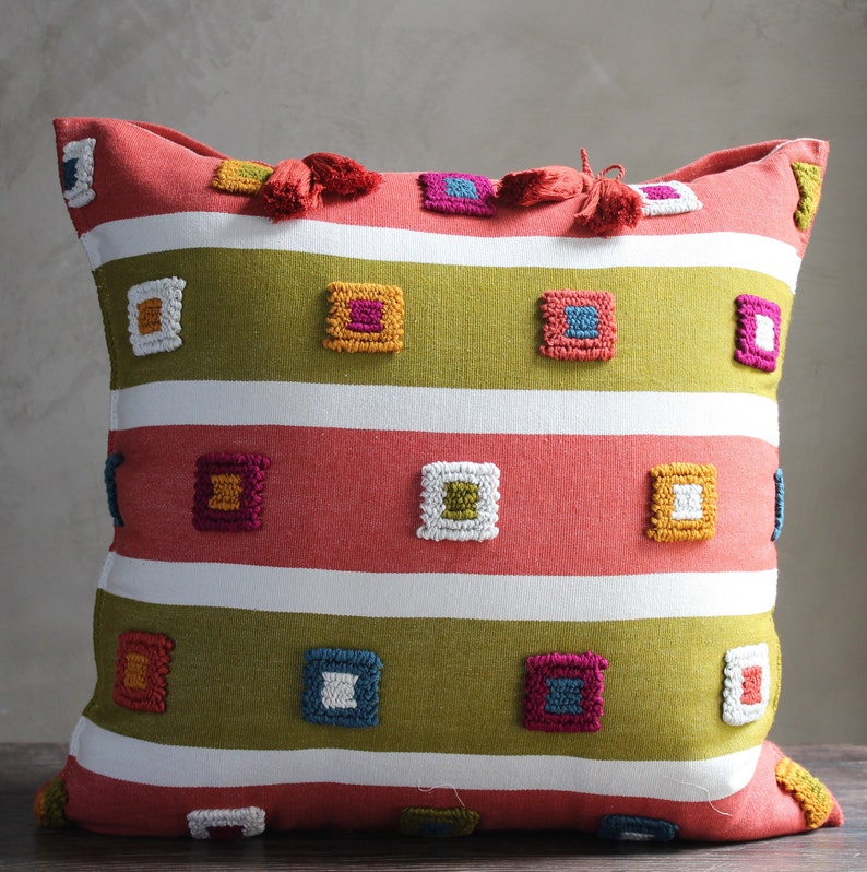 May include: A square throw pillow with a red, white, and green striped pattern. The pillow has colorful embroidered squares in a geometric design.