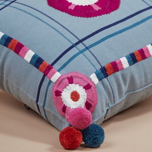 May include: A blue and white plaid throw pillow with pink and white embroidered flowers and pom-poms.