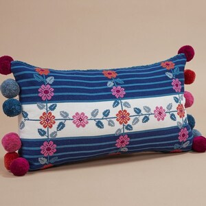May include: A blue and white striped pillow with embroidered pink flowers and green leaves. The pillow has a pom-pom trim in pink and blue.