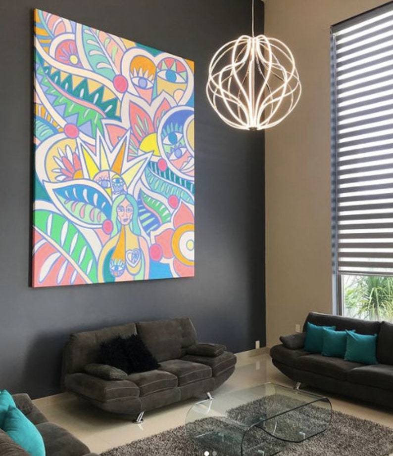 May include: A colorful abstract painting with a woman in the center, surrounded by flowers, leaves, and eyes. The painting is hanging on a dark gray wall in a living room with two gray sofas and a glass coffee table.