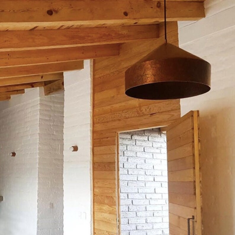 May include: A copper pendant light fixture hangs from a wooden ceiling in a room with white brick walls and a wooden door.